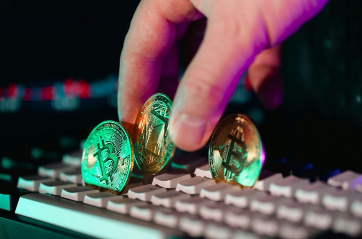 Mão segurando moedas físicas de Bitcoin e Ethereum sobre um teclado de computador.